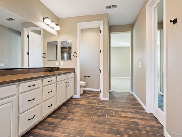 bathroom with toilet, visible vents, wood finished floors, and vanity