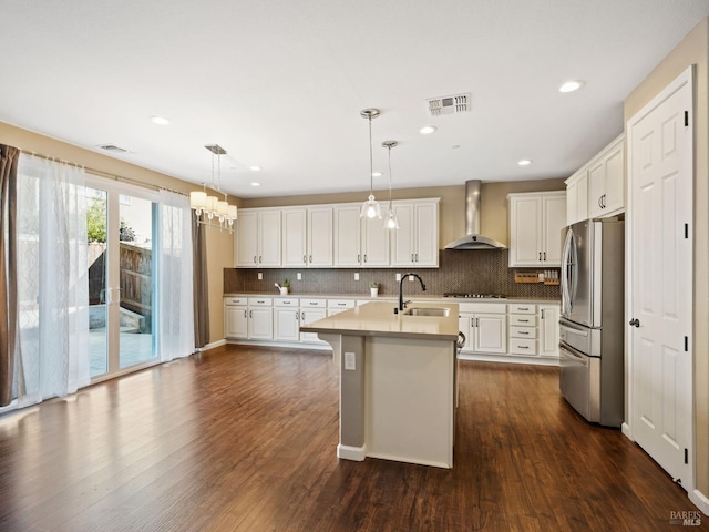 kitchen with gas stovetop, visible vents, a sink, freestanding refrigerator, and wall chimney exhaust hood