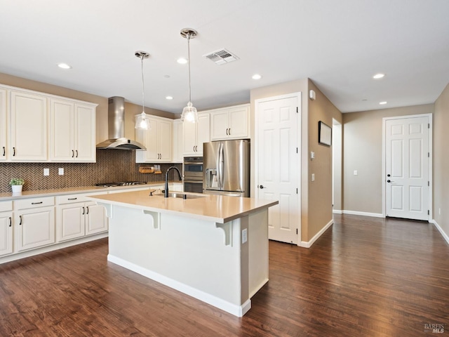 kitchen featuring a center island with sink, visible vents, stainless steel appliances, wall chimney range hood, and a sink