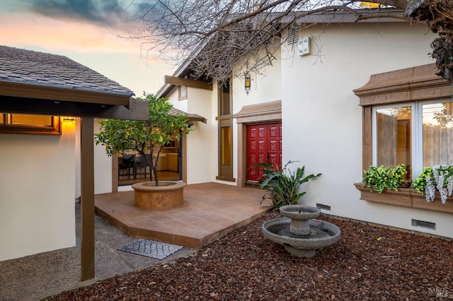 exterior entry at dusk featuring a patio and stucco siding