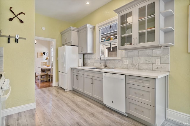 kitchen with tasteful backsplash, gray cabinets, light wood-style floors, a sink, and white appliances