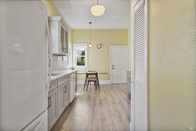 kitchen with light countertops, light wood-type flooring, freestanding refrigerator, glass insert cabinets, and pendant lighting