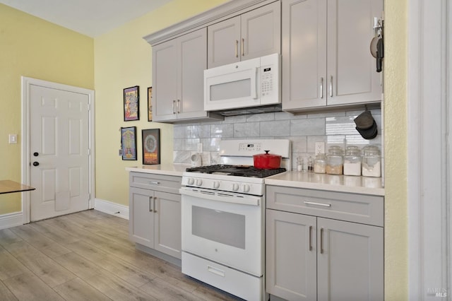 kitchen featuring white appliances, gray cabinets, light wood-style floors, and decorative backsplash