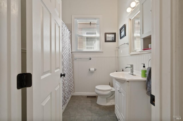 bathroom with wainscoting, toilet, a shower with curtain, tile patterned flooring, and vanity