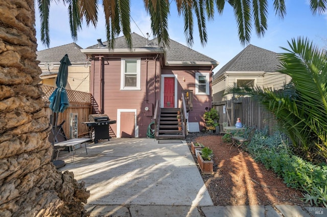 view of front of home featuring roof with shingles, a patio area, and fence