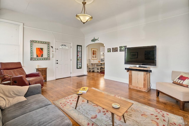 living room featuring arched walkways, baseboards, wood finished floors, and lofted ceiling