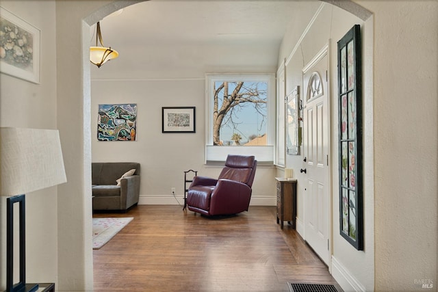 sitting room with arched walkways, visible vents, baseboards, and wood finished floors