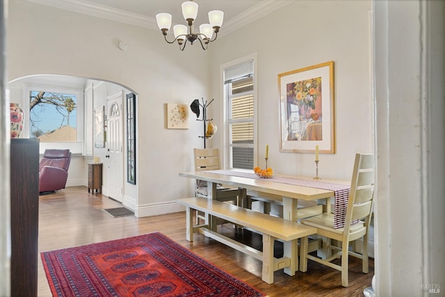 dining room with arched walkways, an inviting chandelier, ornamental molding, wood finished floors, and baseboards