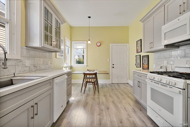 kitchen featuring light countertops, light wood-style flooring, a sink, white appliances, and baseboards