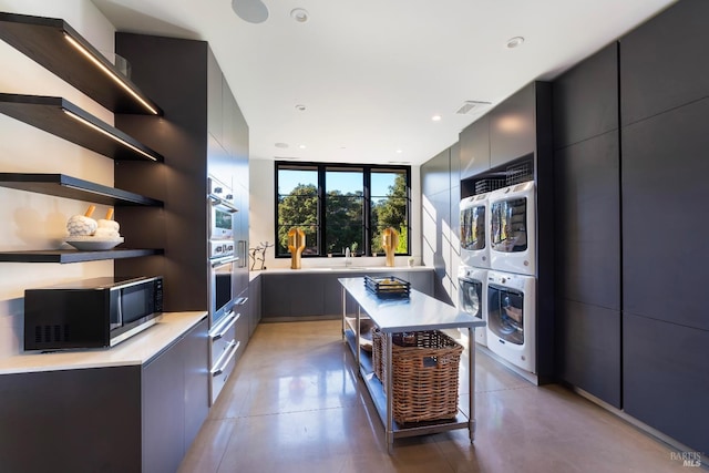 kitchen with black microwave, open shelves, and stacked washer and clothes dryer