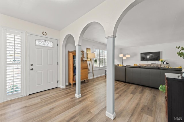 entryway with light wood-type flooring, ornate columns, baseboards, and arched walkways