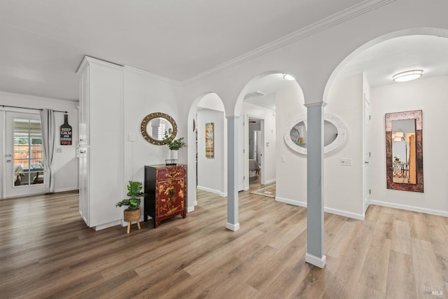 interior space with light wood-style floors, baseboards, ornamental molding, and arched walkways