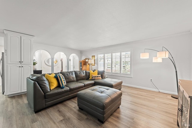 living room with light wood-style flooring, arched walkways, baseboards, and ornamental molding