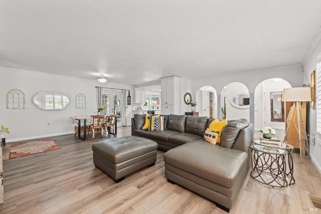 living room with light wood finished floors, baseboards, arched walkways, and crown molding