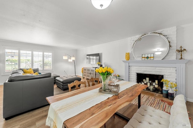 dining space with light wood-type flooring, a fireplace, baseboards, and crown molding