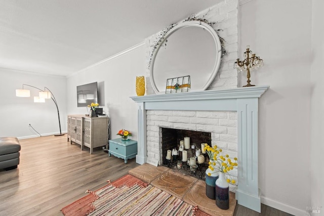 living room with a brick fireplace, crown molding, baseboards, and wood finished floors