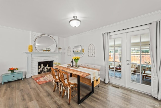 dining space featuring french doors, crown molding, a fireplace, visible vents, and wood finished floors