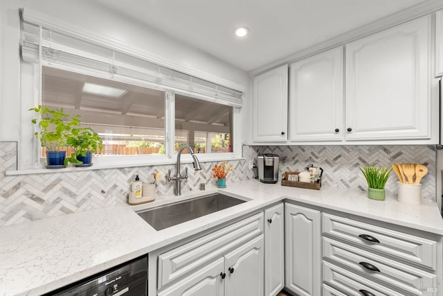 kitchen featuring light stone counters, backsplash, white cabinets, a sink, and dishwashing machine