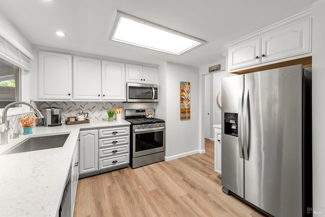 kitchen featuring light wood finished floors, stainless steel appliances, decorative backsplash, white cabinets, and a sink