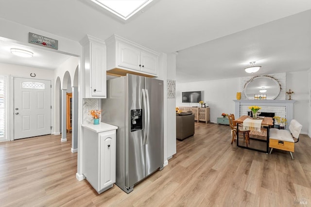 kitchen featuring arched walkways, a fireplace, white cabinetry, light countertops, and stainless steel fridge