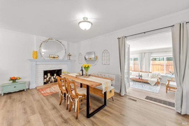 dining area with a fireplace, visible vents, baseboards, ornamental molding, and light wood finished floors