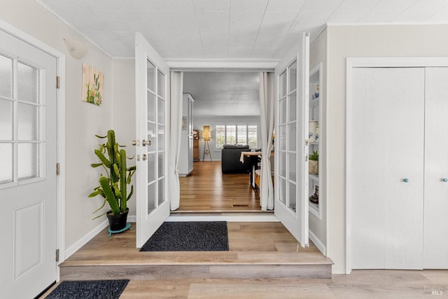 entrance foyer with ornamental molding, french doors, baseboards, and wood finished floors