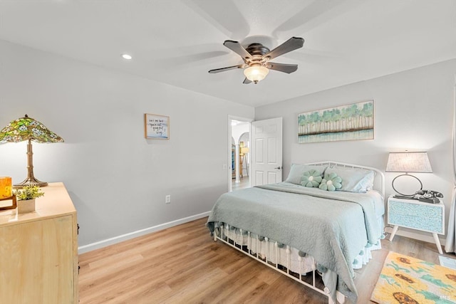 bedroom with light wood-type flooring, ceiling fan, arched walkways, and baseboards