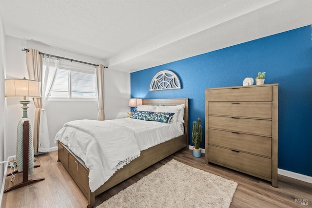 bedroom with a textured wall, a textured ceiling, baseboards, and wood finished floors