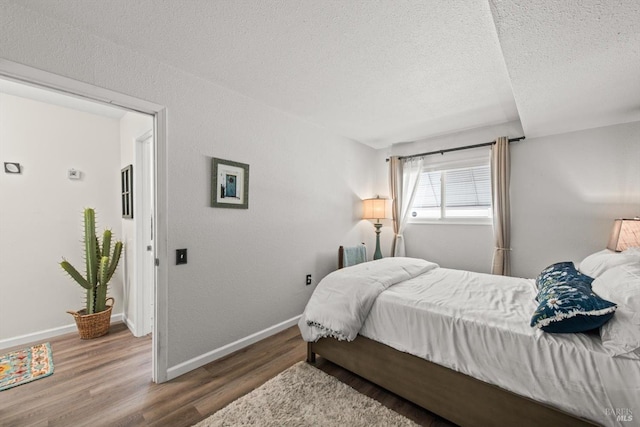 bedroom with a textured ceiling, baseboards, and wood finished floors