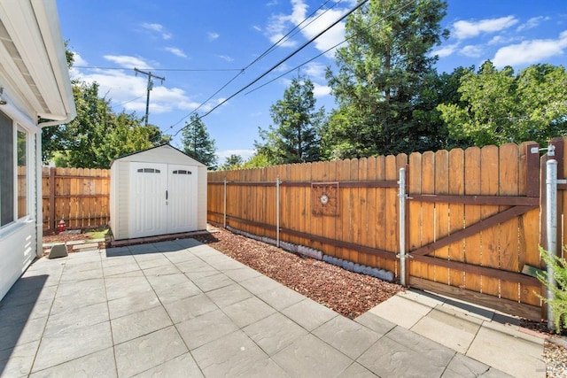 view of patio / terrace with a storage shed, an outdoor structure, a fenced backyard, and a gate