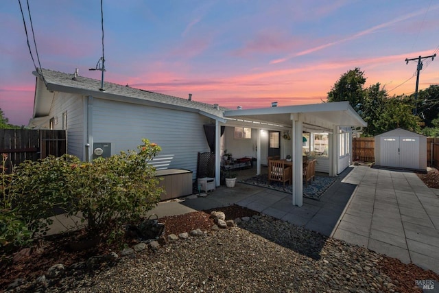 rear view of property with a storage shed, a patio area, fence, and an outbuilding