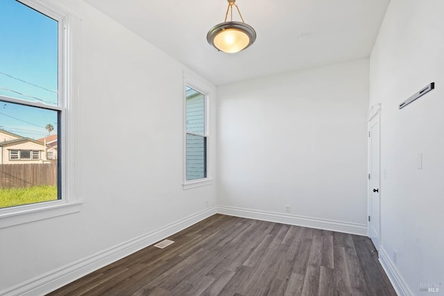 empty room with dark wood finished floors, visible vents, and baseboards