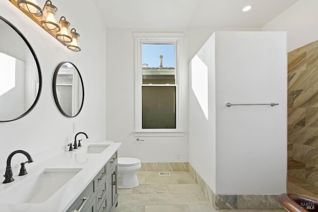 full bathroom featuring a tile shower, double vanity, a sink, and toilet