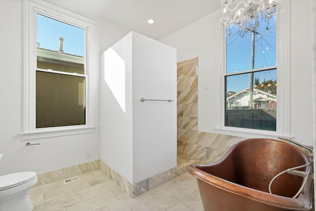 bathroom with a freestanding tub, toilet, a notable chandelier, visible vents, and tile patterned floors