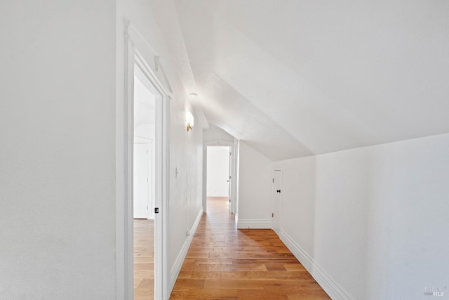 corridor featuring light wood-type flooring, baseboards, and vaulted ceiling