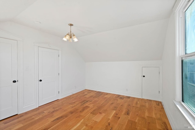 additional living space with lofted ceiling, light wood-type flooring, baseboards, and an inviting chandelier