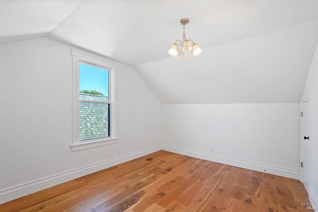 additional living space featuring vaulted ceiling, light wood finished floors, an inviting chandelier, and baseboards