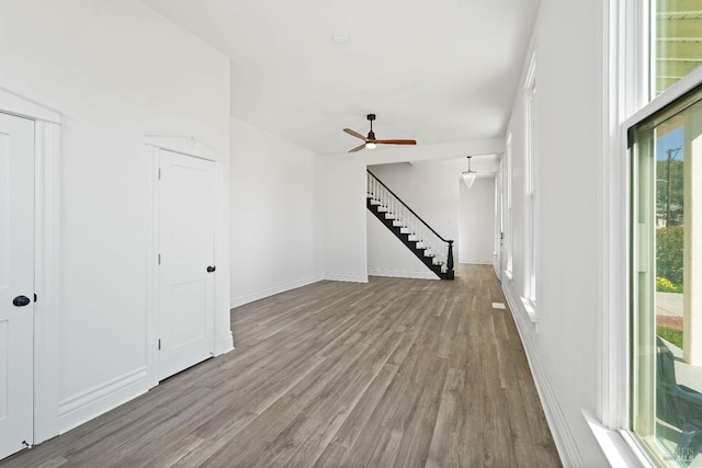 unfurnished living room with stairs, ceiling fan, baseboards, and wood finished floors