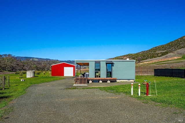 manufactured / mobile home with aphalt driveway, a detached garage, a mountain view, an outdoor structure, and a front lawn