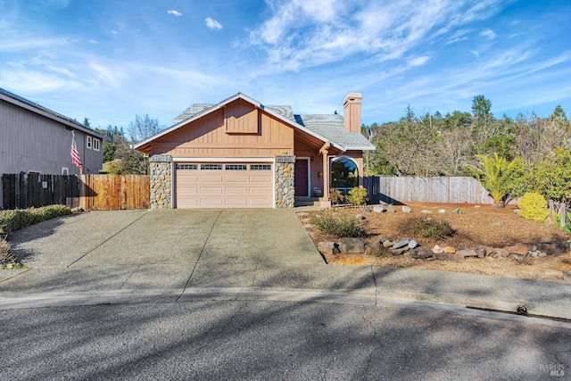 view of front of house with a garage, driveway, stone siding, a chimney, and fence