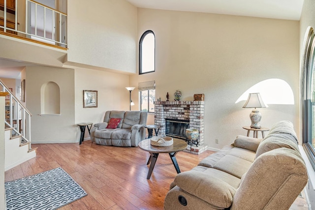 living area with a towering ceiling, a brick fireplace, and hardwood / wood-style floors