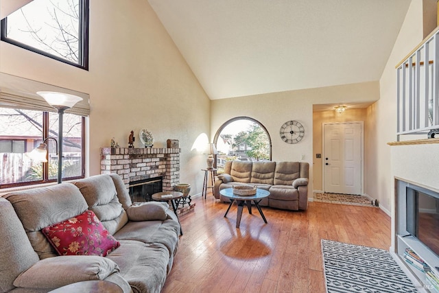 living area featuring high vaulted ceiling, hardwood / wood-style floors, a fireplace, and baseboards