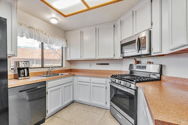 kitchen with light tile patterned floors, appliances with stainless steel finishes, light countertops, white cabinetry, and a sink