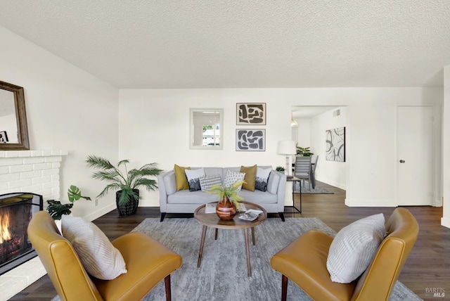 living room with a brick fireplace, a textured ceiling, baseboards, and wood finished floors