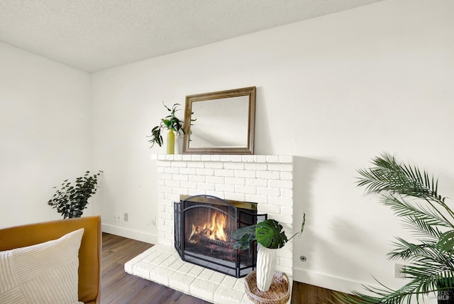 living area with a fireplace, a textured ceiling, baseboards, and wood finished floors