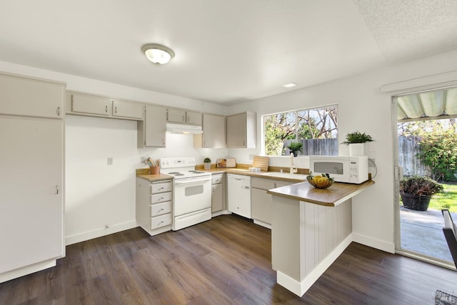 kitchen featuring white appliances, dark wood-type flooring, a peninsula, under cabinet range hood, and a sink