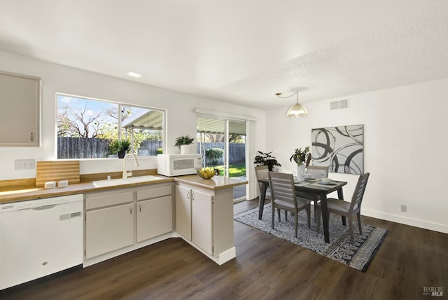 kitchen with white appliances, a sink, visible vents, light countertops, and dark wood-style floors