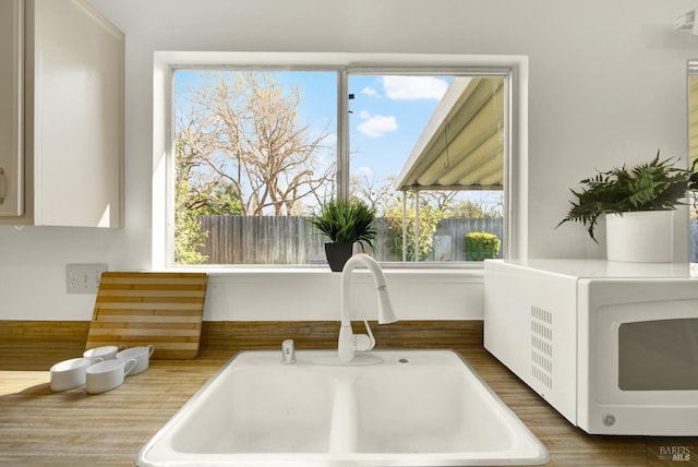 details featuring white cabinets, white microwave, light countertops, and a sink