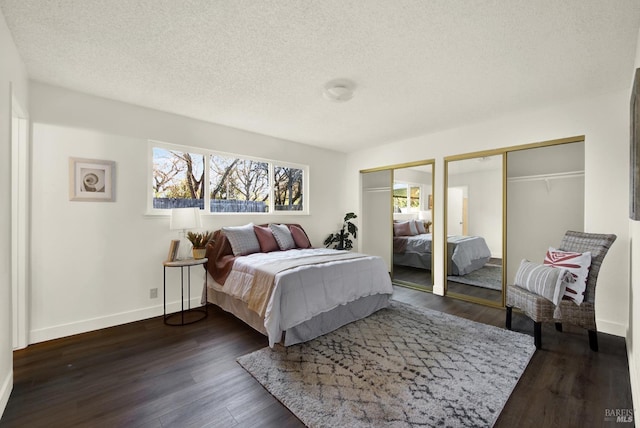 bedroom featuring dark wood finished floors, a textured ceiling, baseboards, and two closets