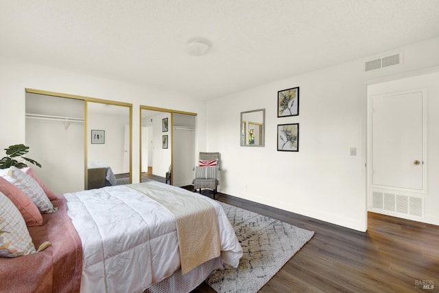 bedroom with baseboards, wood finished floors, visible vents, and multiple closets